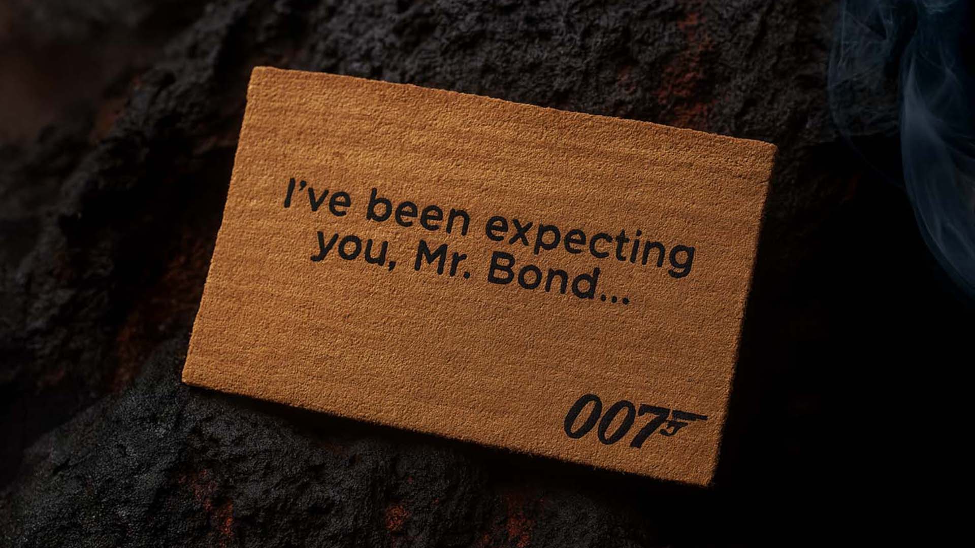 Official James Bond 007 doormat with the quote “I’ve been expecting you, Mr. Bond…” placed on a rugged lava stone ground.